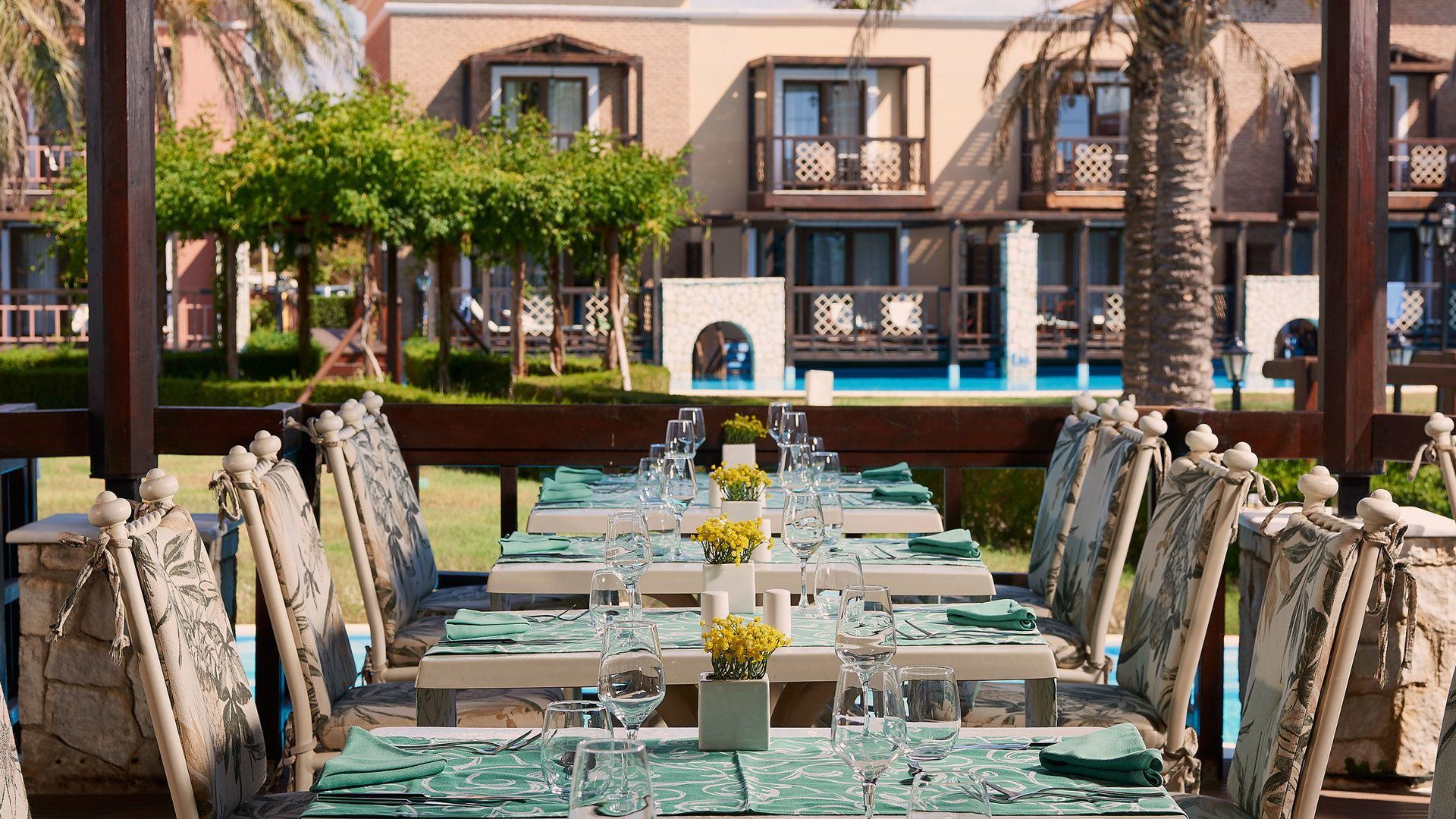 Tables set with green linens and yellow flowers, wicker chairs and a view of gardens, palm trees and the pool