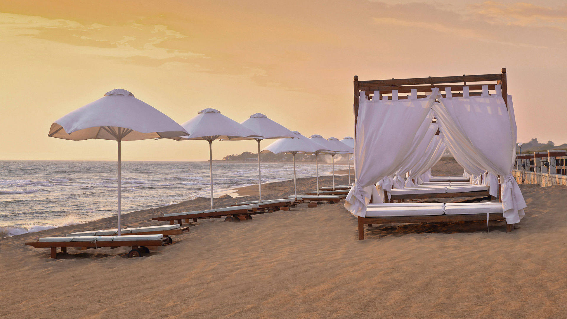 Sunbeds, white umbrellas and a gazebo lounger on Skafidia beach in golden sunset light at Aldemar Olympian Village