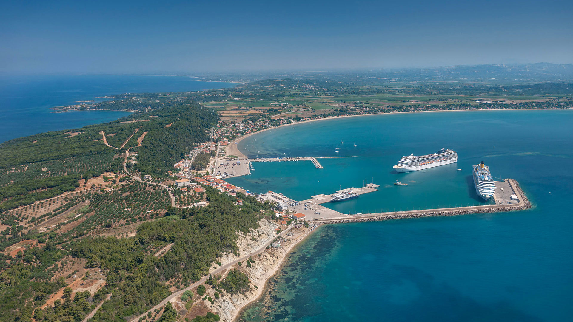 Aerial view of Katakolo port with cruise ships docked in the bay, surrounded by green hills and blue sea