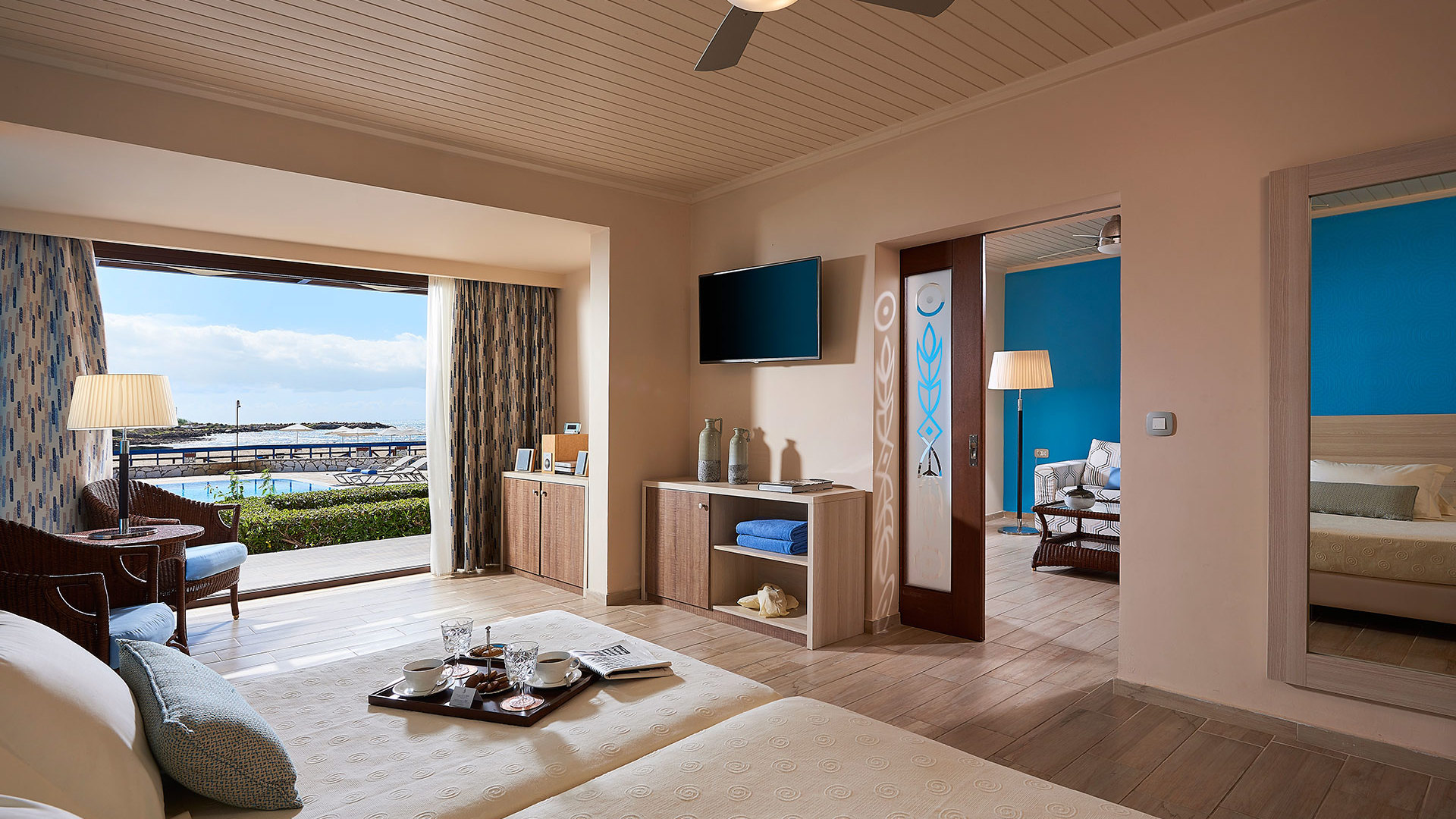 Bedroom with a tray on the bed, ceiling fan, TV, door to a second blue bedroom and open doors to a terrace with sea view