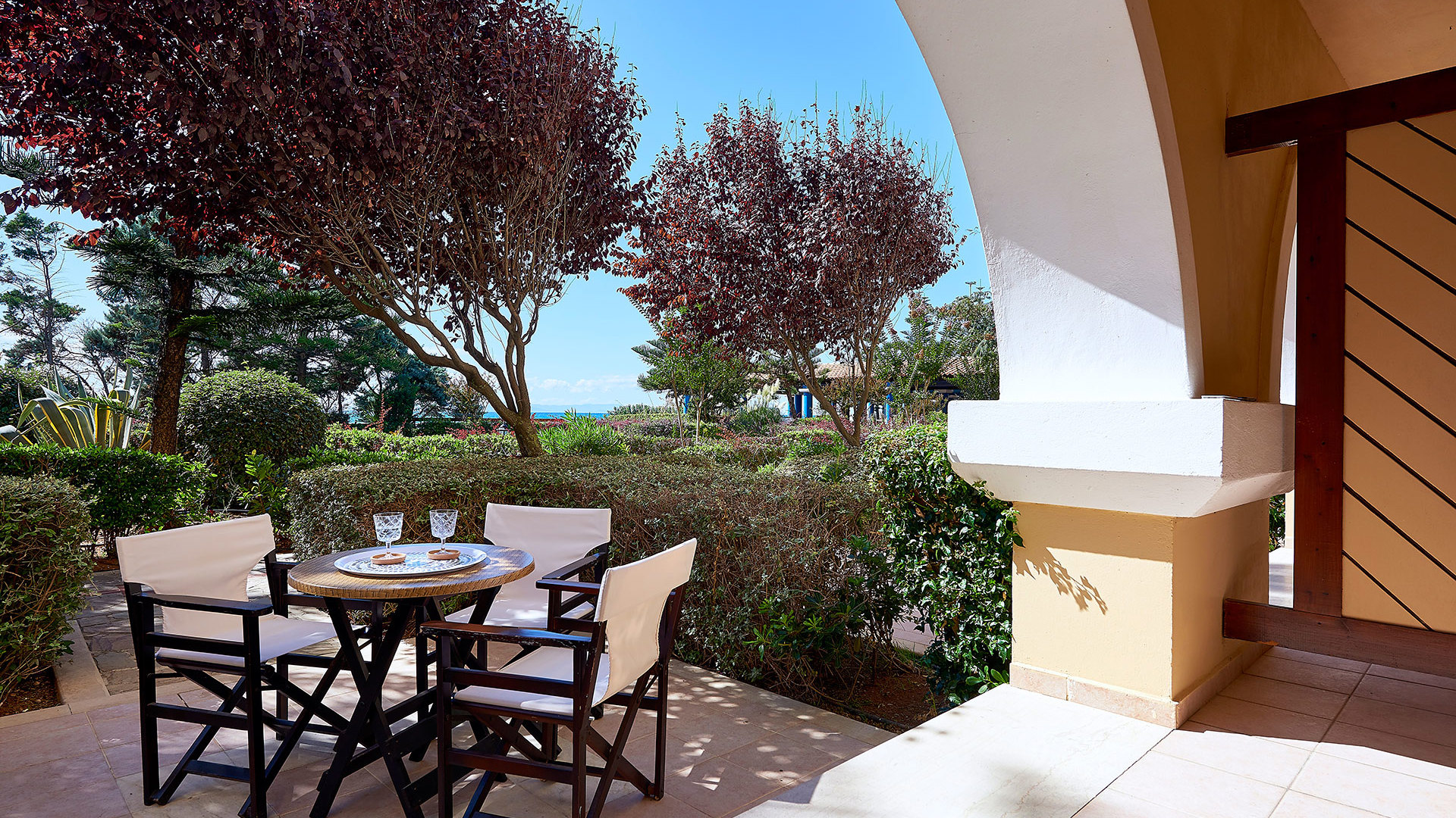 Balcony of Main Building Double Room Garden View with table and chairs overlooking lush gardens at Aldemar Olympian Village