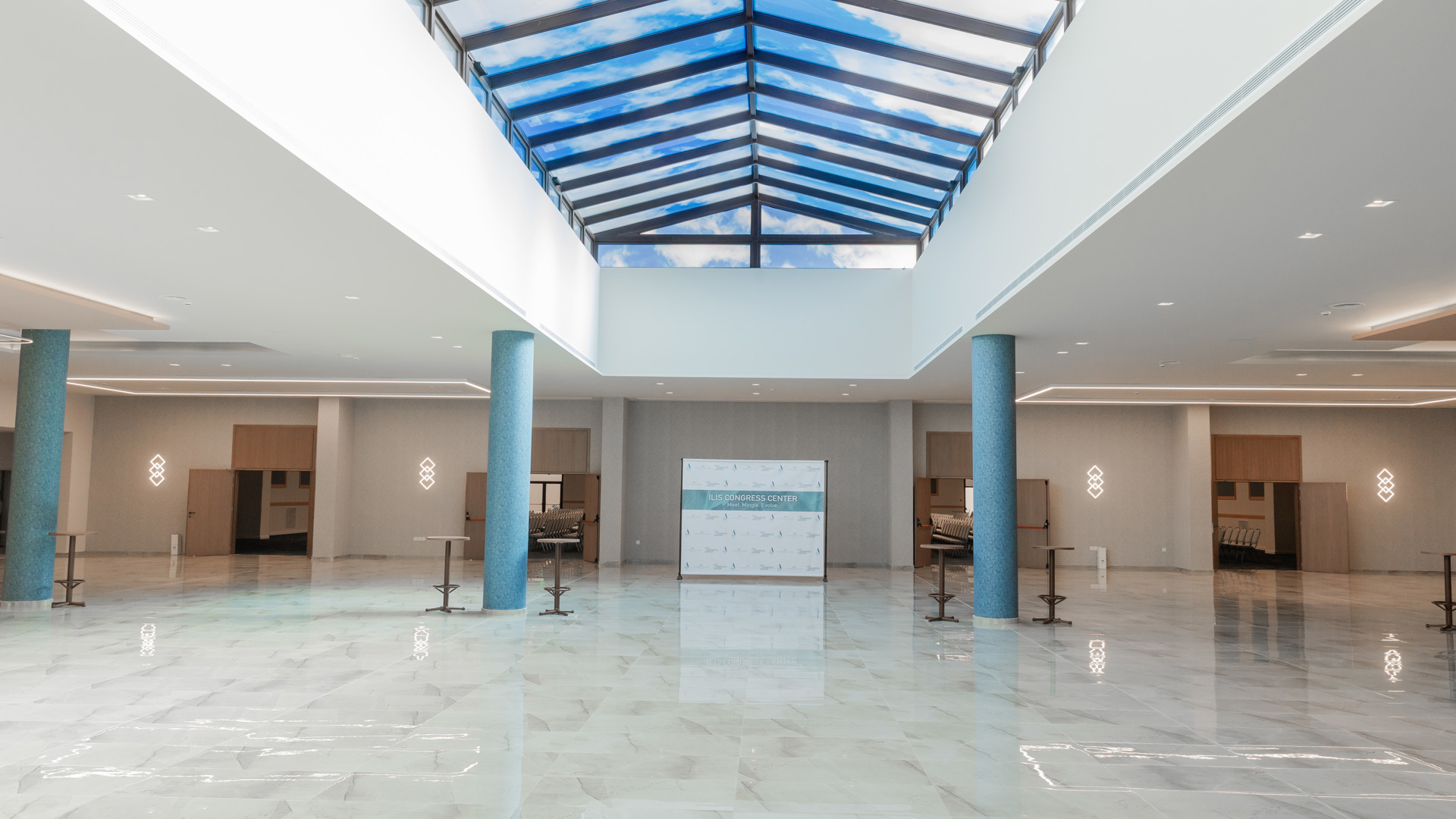 Spacious foyer under a large glass skylight, with a polished marble floor, blue columns and a registration desk