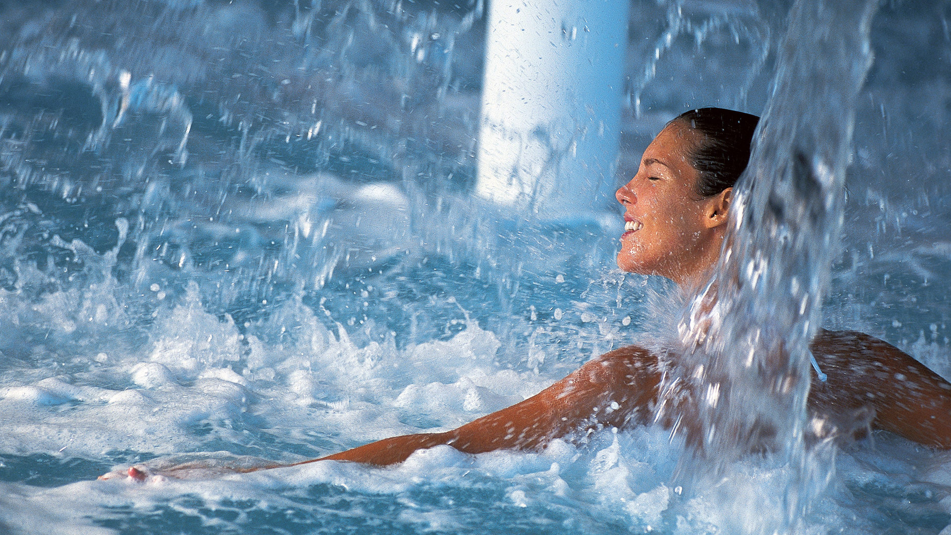 Smiling woman enjoying the splashing water jets of a hydrotherapy pool, her arm stretched out on the surface