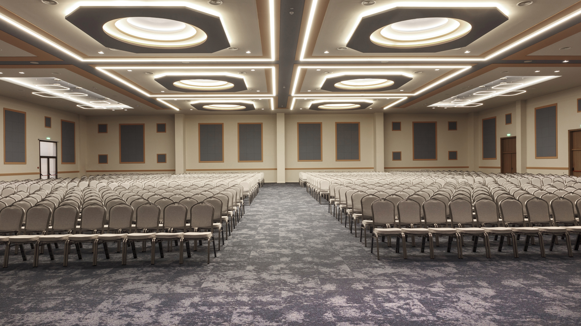 Large hall with hundreds of beige chairs set in two blocks, a central aisle and an illuminated geometric ceiling